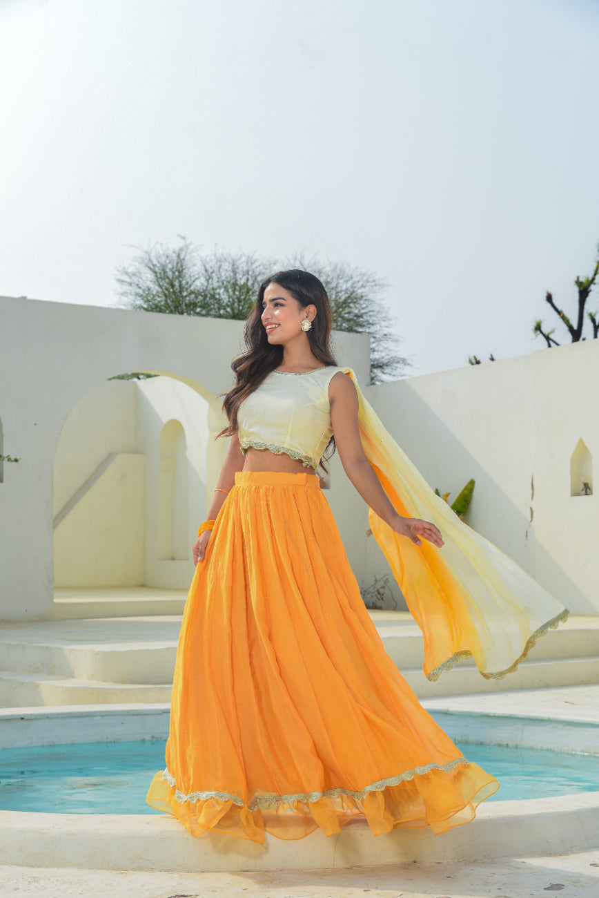 Woman in a yellow and white traditional outfit standing by a pool with a white building in the background.