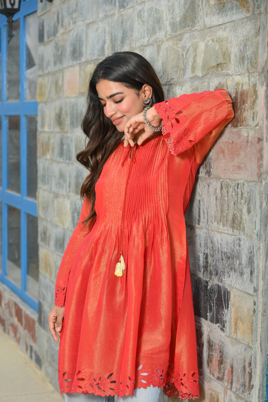 Woman in a red dress leaning against a stone wall.