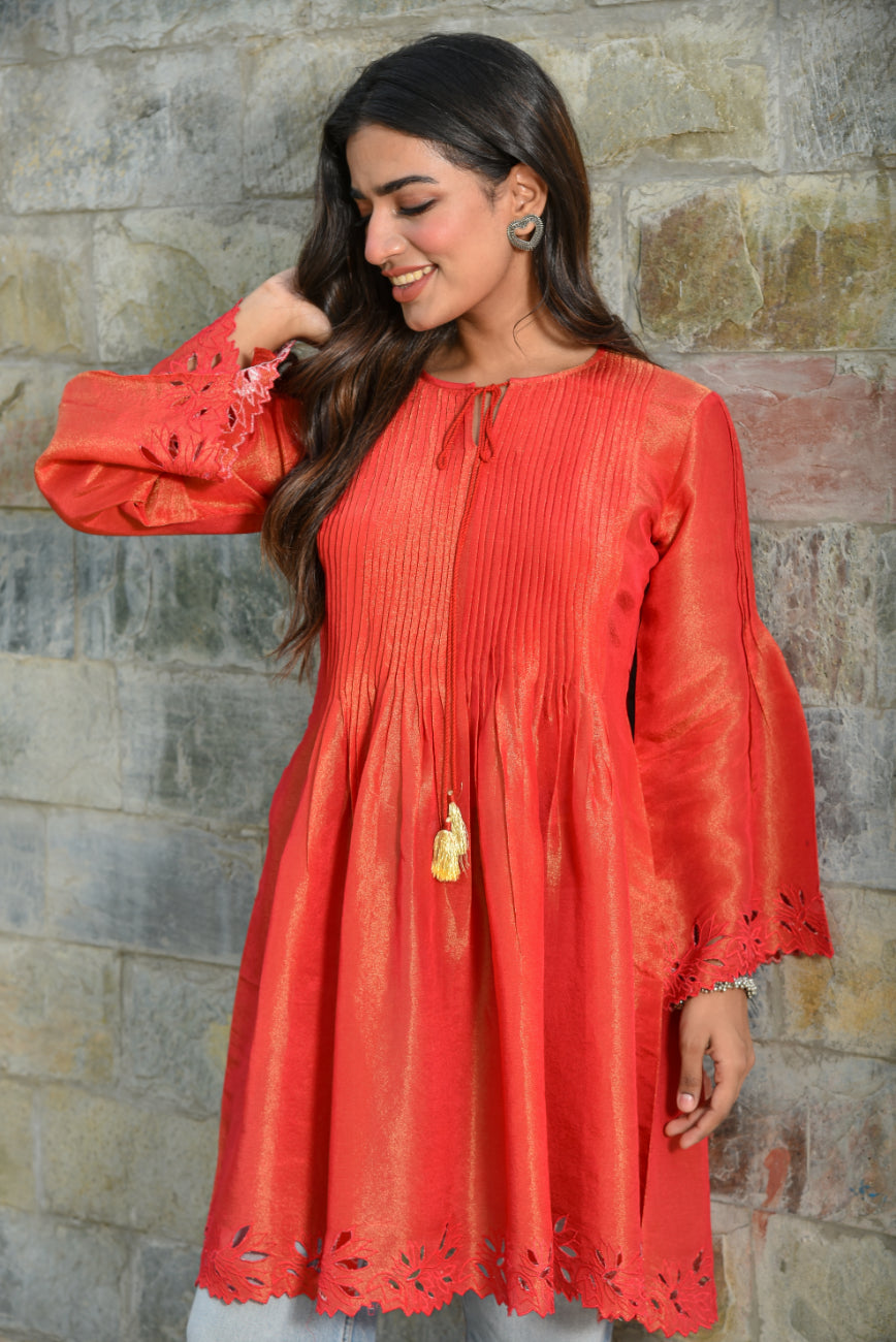 Woman wearing a red dress with long sleeves against a stone wall.