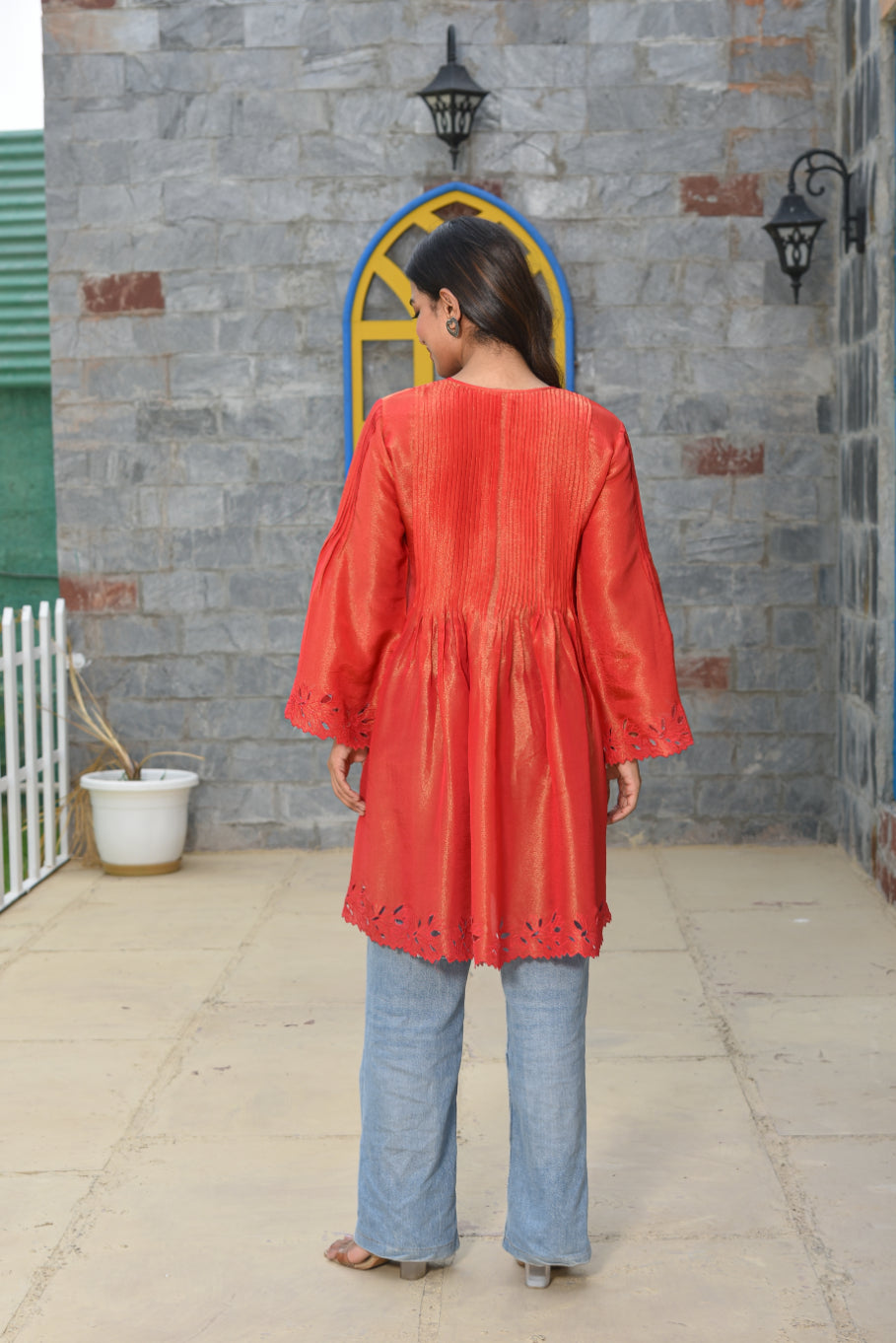 Person wearing a red top and blue pants standing in front of a stone wall.