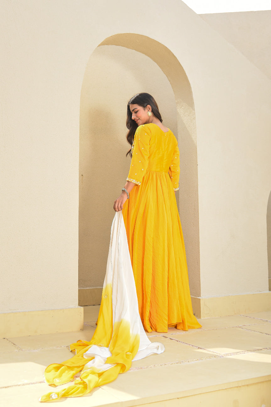 Woman in a yellow dress holding a white scarf in a sunlit room with arches.