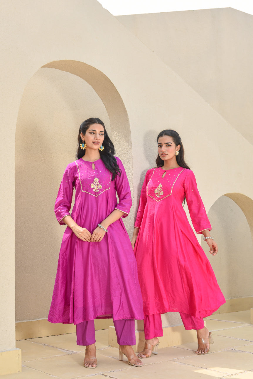 Two women wearing pink traditional outfits standing in front of beige arches.
