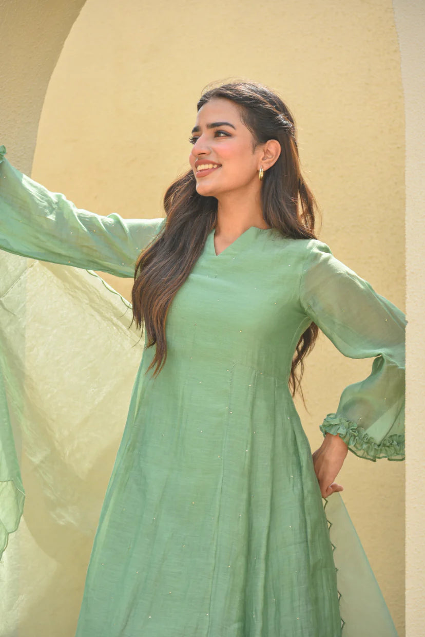 The Mukesh Work A-line Kurta Set by Asya by Saroj Jain is a stunning and elegant ensemble that exudes sophistication and refinement. Crafted from premium Mal Chanderi, this set features an exquisite A-line kurta adorned with delicate, hand-crafted Mukesh work that catches the light beautifully. The kurta's A-line silhouette is both flattering and comfortable, while the ruffled sleeves add a touch of whimsy and romance.