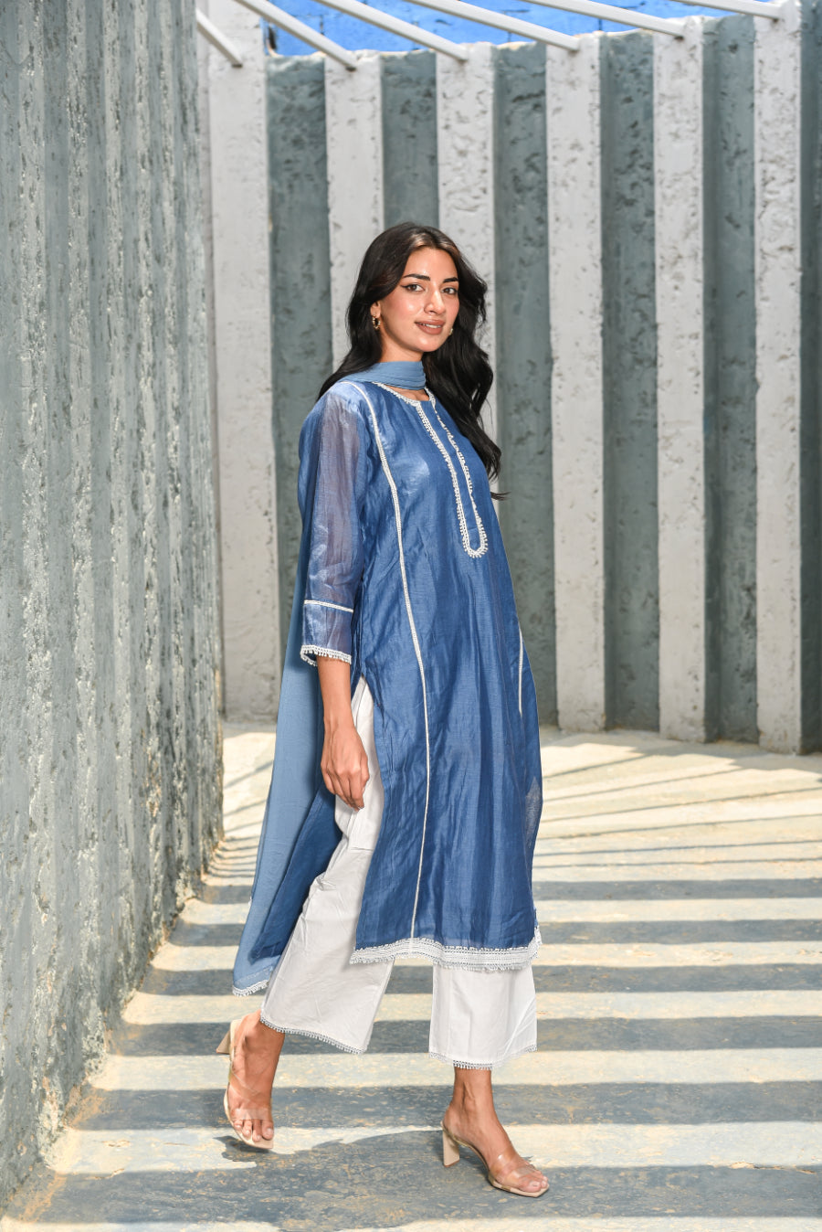 Woman wearing a blue kurta with white pants standing on stone steps.