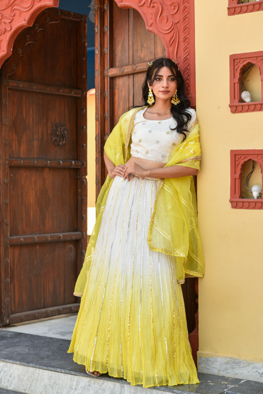 Woman in a yellow and white traditional outfit standing in front of a decorative door.