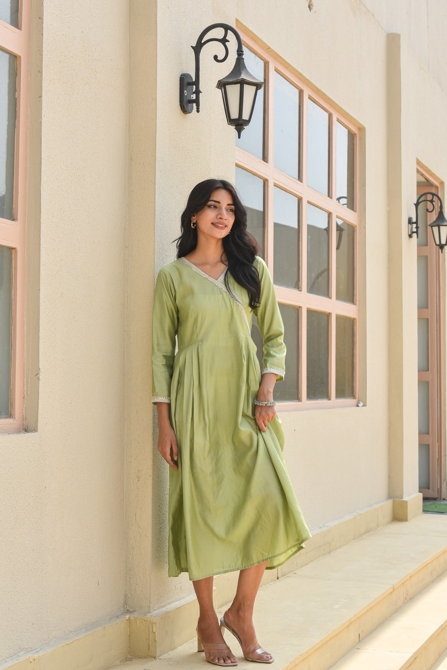 Woman in a green dress standing outside a building with large windows.