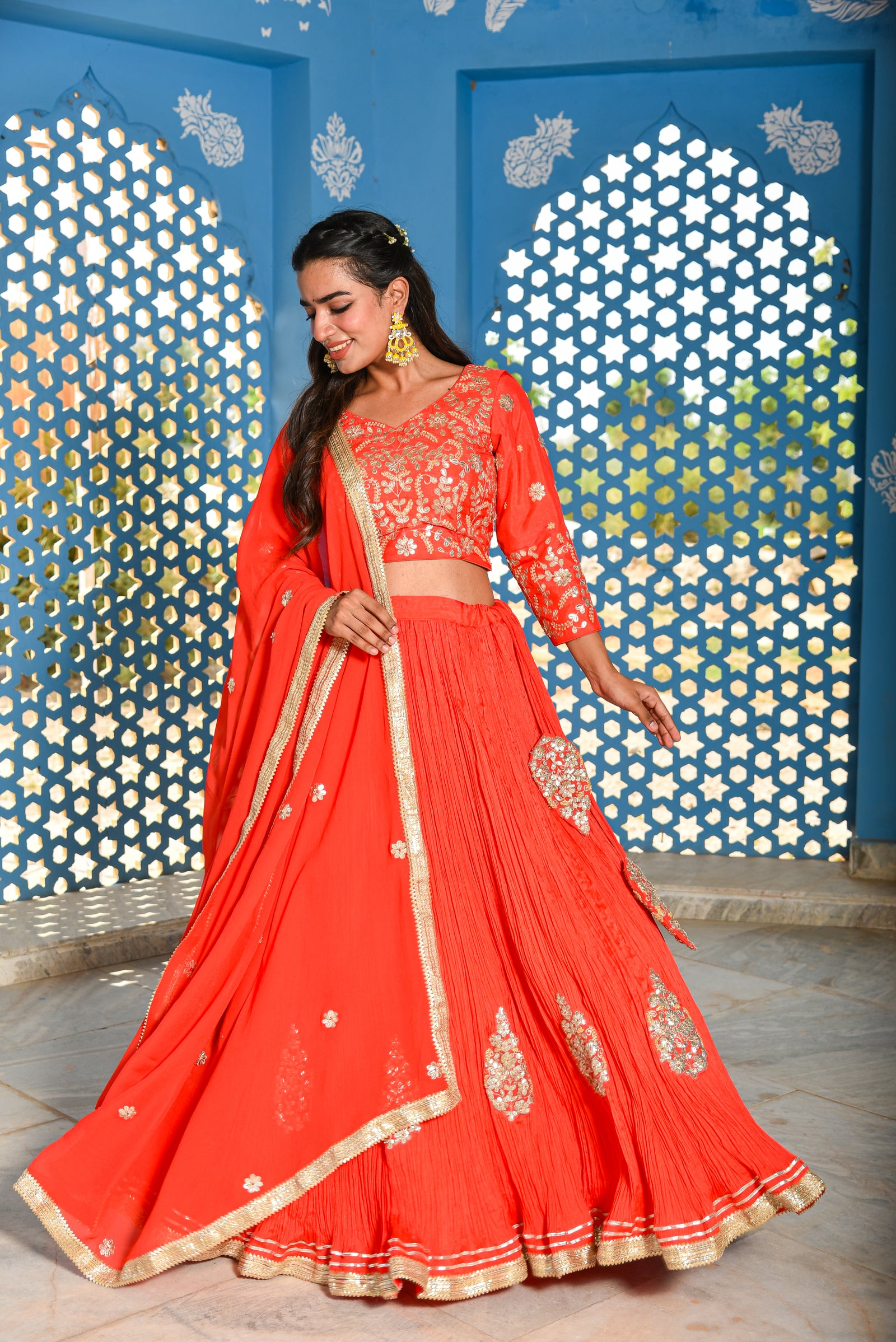 Woman in a red traditional outfit with gold details against a decorative blue wall.