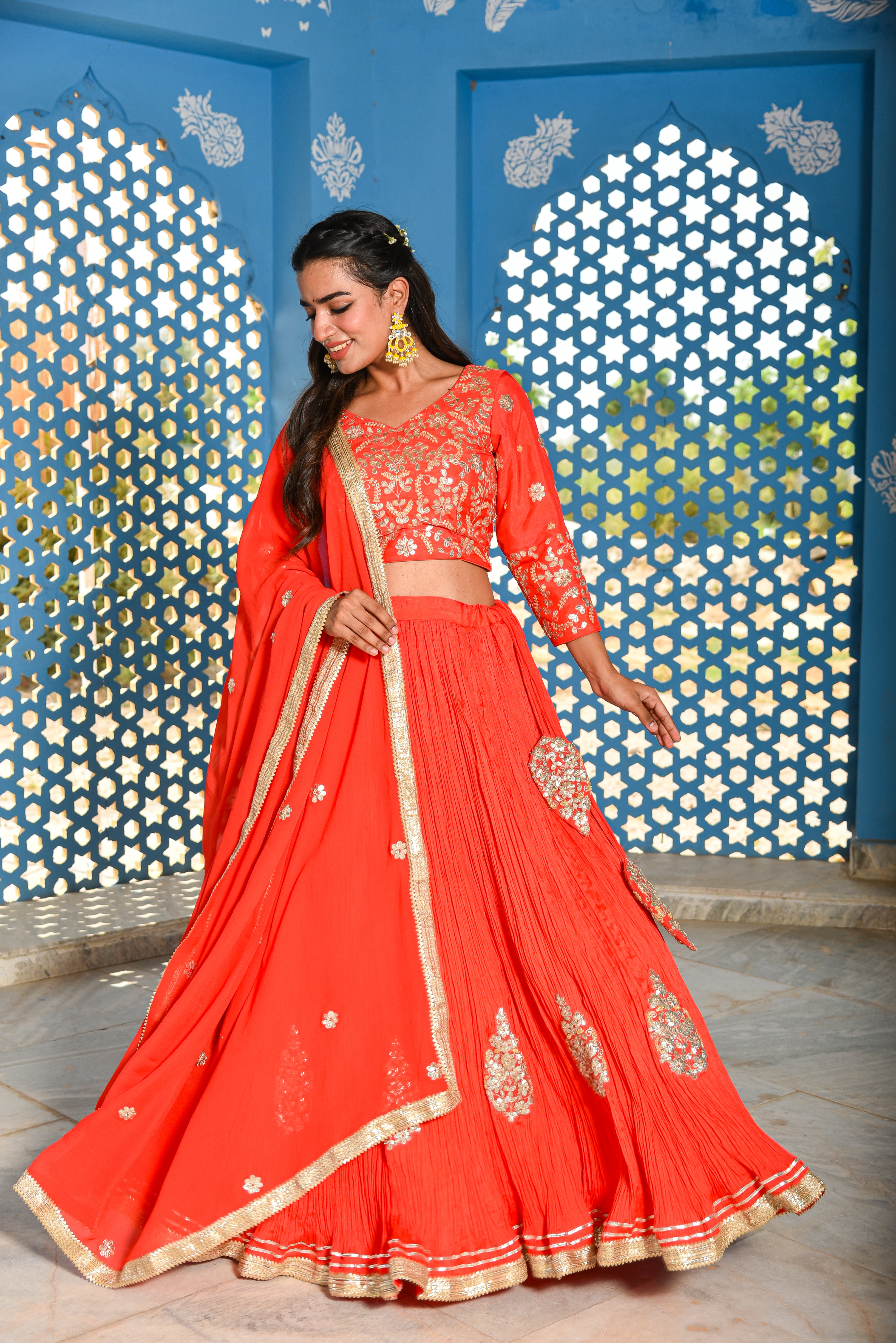 Woman in a red traditional outfit with gold details against a decorative blue wall.