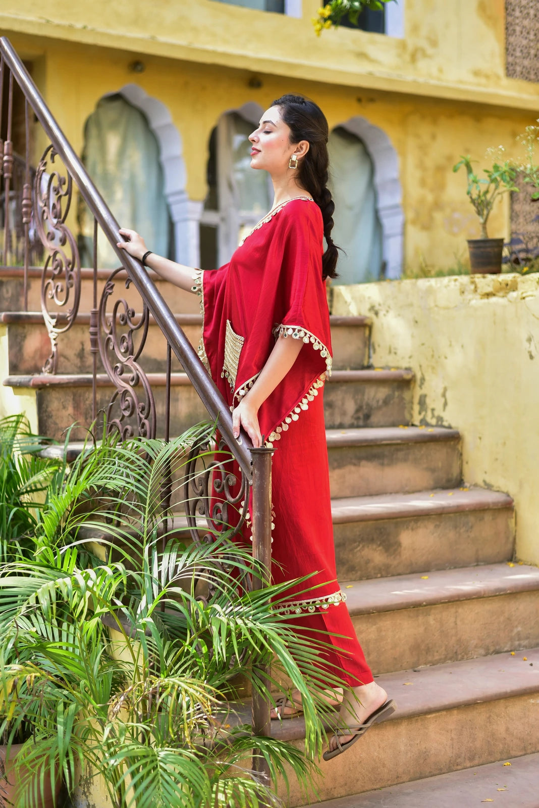 The image showcases a woman in a stunning red kaftan, a traditional Middle Eastern garment, exuding elegance and sophistication. The kaftan features a vibrant red hue, complemented by intricate gold embroidery that adds a touch of luxury to the overall design. Its loose-fitting silhouette, adorned with a high neckline and short sleeves, creates a sense of fluidity and movement, while the long, flowing length adds drama and flair.

The kaftan's fabric appears to be lightweight and breathable, making it an id