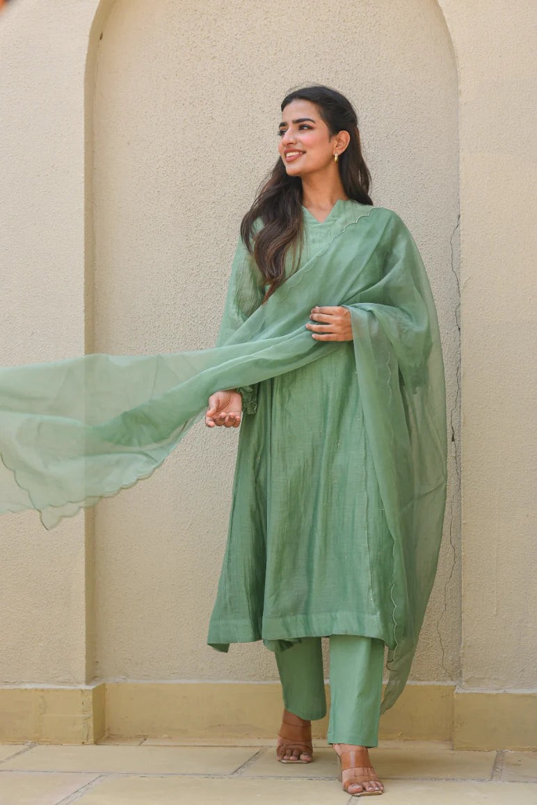This fern green Mal Chanderi set features an A-line kurta with a slit neckline and full sleeves, adorned with delicate Mukesh work. It includes a comfortable cotton pant with a half-elastic waist and pull-up closure, paired with a graceful organza dupatta—perfect for festive and elegant occasions.