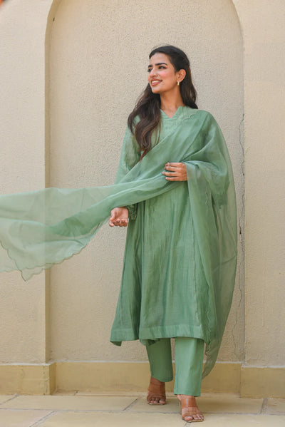This fern green Mal Chanderi set features an A-line kurta with a slit neckline and full sleeves, adorned with delicate Mukesh work. It includes a comfortable cotton pant with a half-elastic waist and pull-up closure, paired with a graceful organza dupatta—perfect for festive and elegant occasions.