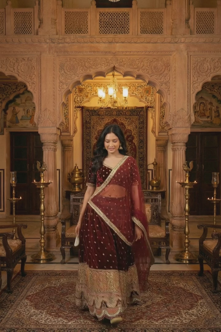 Velvet Lehenga Set by Saroj Jain, designed for women who embrace heritage with confidence and grace. Crafted in rich maroon velvet, this ensemble captures the grandeur of royal Indian artistry while maintaining a refined, contemporary silhouette.