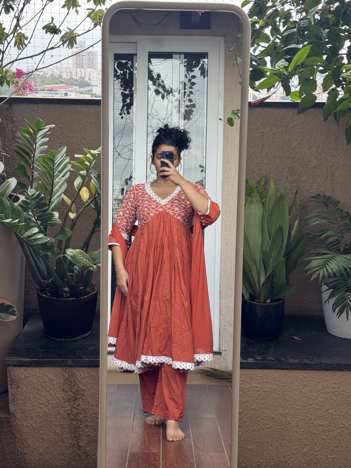 Saroj Jain Terracotta Rust Red Lucknowi Chikankari Anarkali Gown front view showing white thread embroidery and scalloped lace hem.